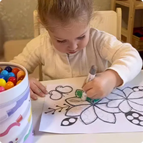 Toddler coloring next to a bucket of colorful beads