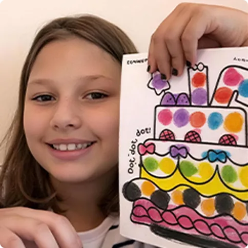 Child holding up a dot-marker cake artwork