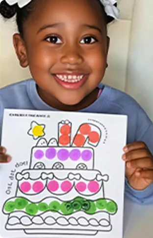 Child holding a dot-marker artwork beside colorful play balls